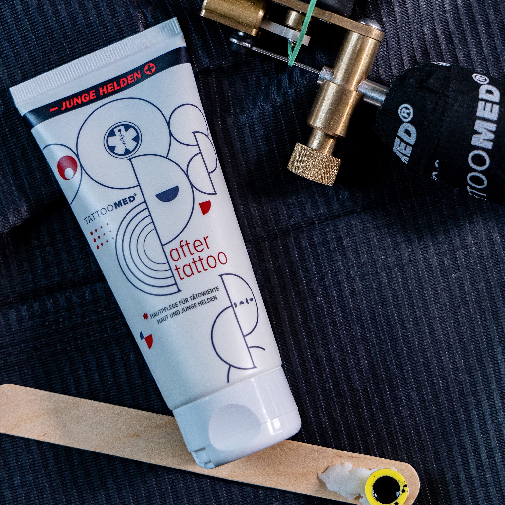 TattooMed® After Tattoo x Junge Helden Special Edition neben einer Tätowiermaschine auf einem schwarzen Hintergrund