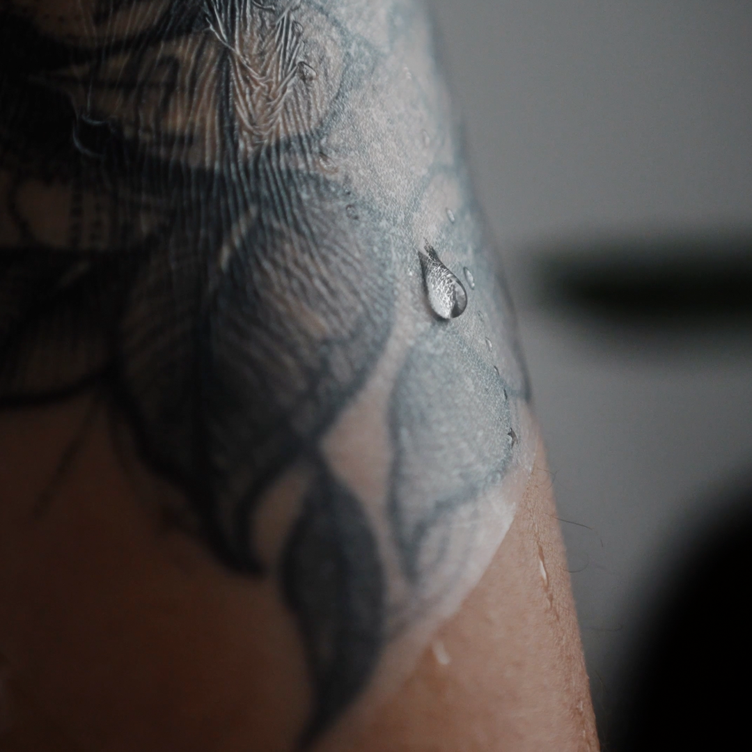 TattooMed Protection Film auf tätowierter Haut. Wassertropfen läuft am Film herunter.